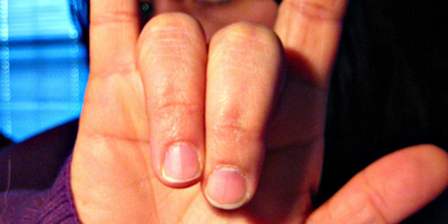 Een vrouw in een paarse trui met zwart haar, laat een 'rock and roll' teken zien met haar hand.