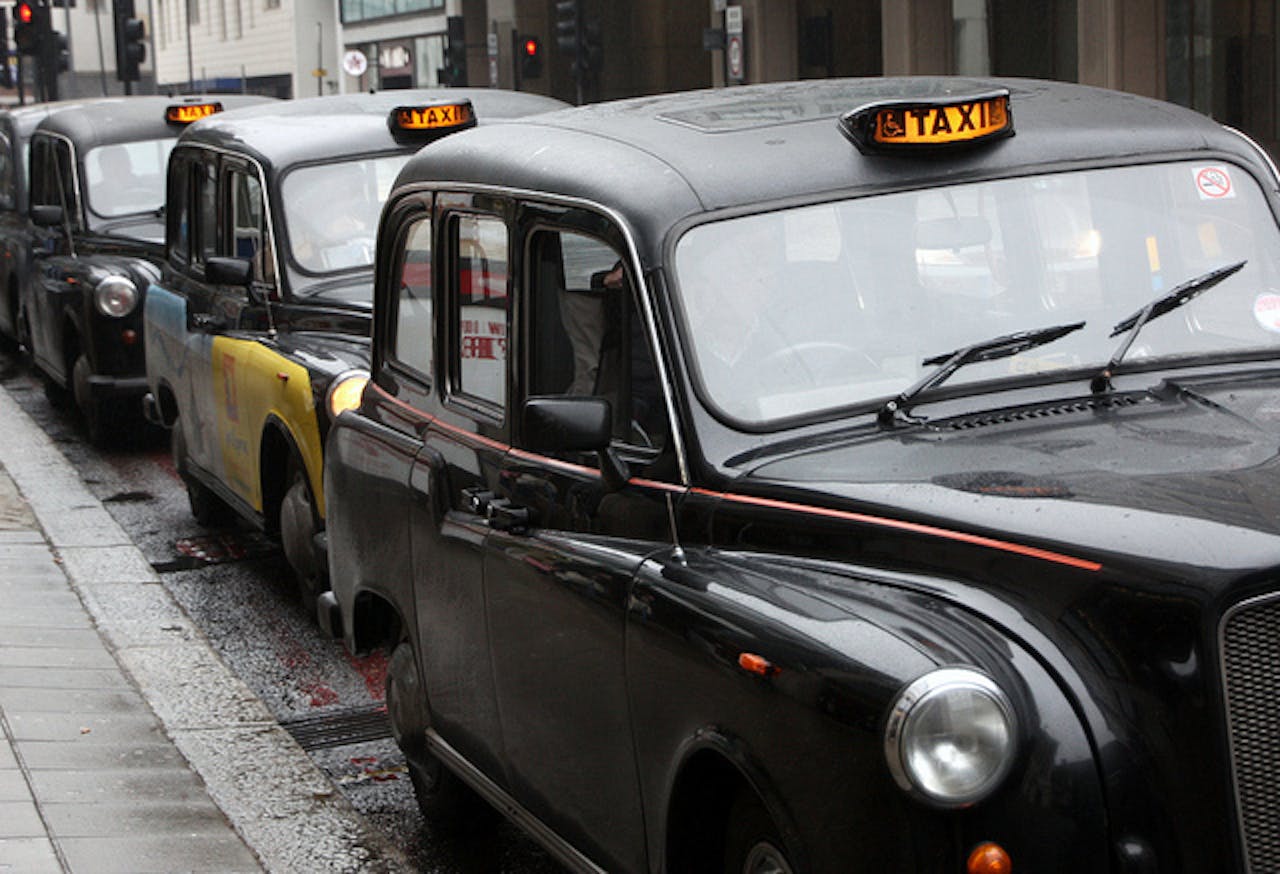 Een rij zwarte taxi's geparkeerd in een natte straat.