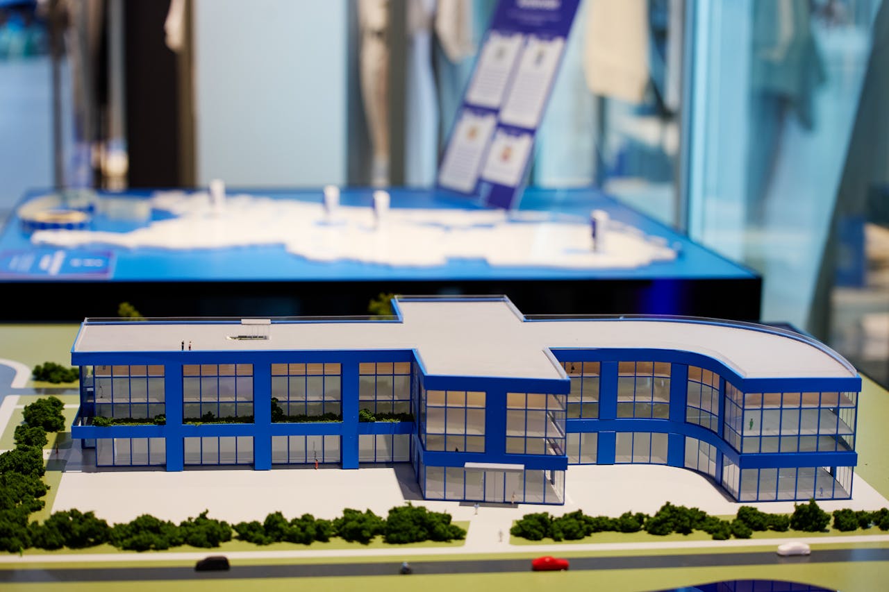 Een maquette op een tafel van een gebouw in de vorm van een f, met veel glas en blauwe wanden. Het platte dak is grijs.