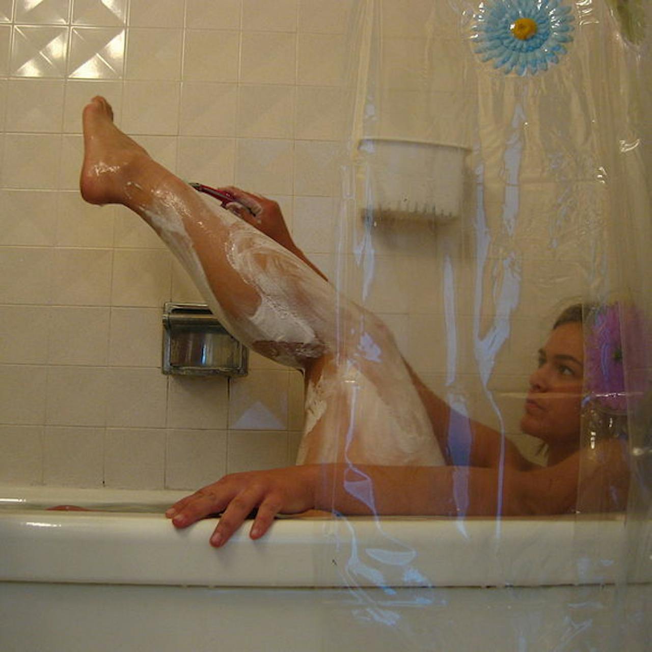 Een vrouw scheert haar benen in een badkuip.
