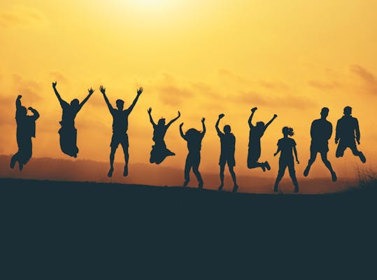 Silhouet van tien mensen die in de lucht springen tegen de achtergrond van een ondergaande zon