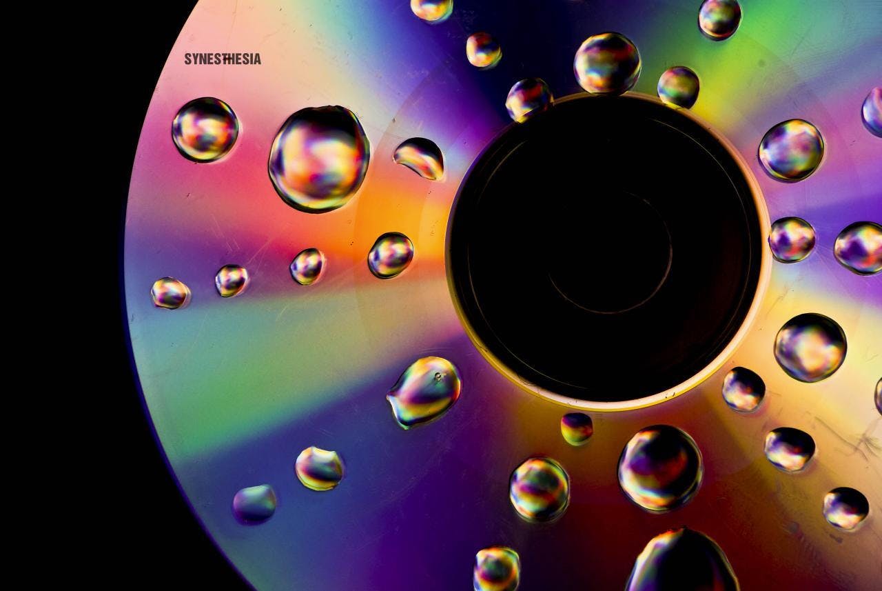 Een cd met waterdruppels en het woord 'Synesthesia' erop. Synesthesie is een eigenschap van de hersenen waarbij de waarneming van het ene zintuig onwillekeurig verbonden wordt met die van een ander zintuig.