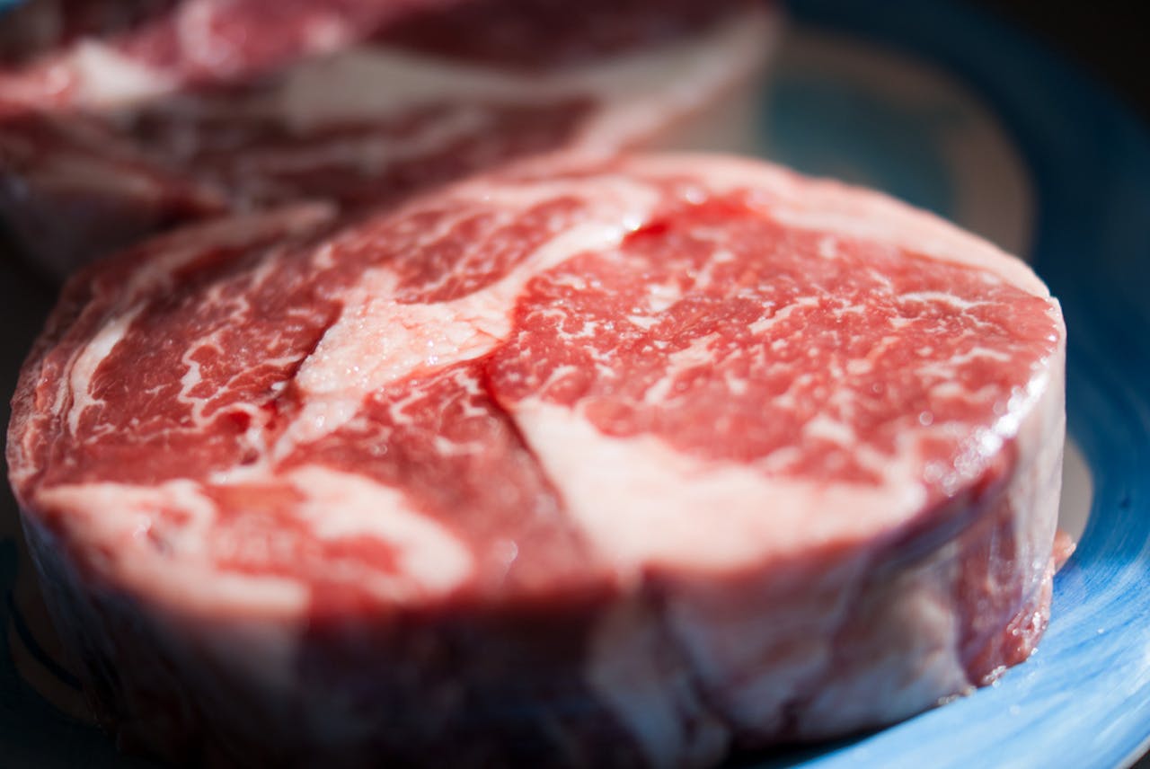 Dierlijke producten drukken zwaar op het milieu. Gemiddeld eten Nederlanders 100 gram vlees en 15 gram vis per dag. Een stuk vlees op een blauw bord.