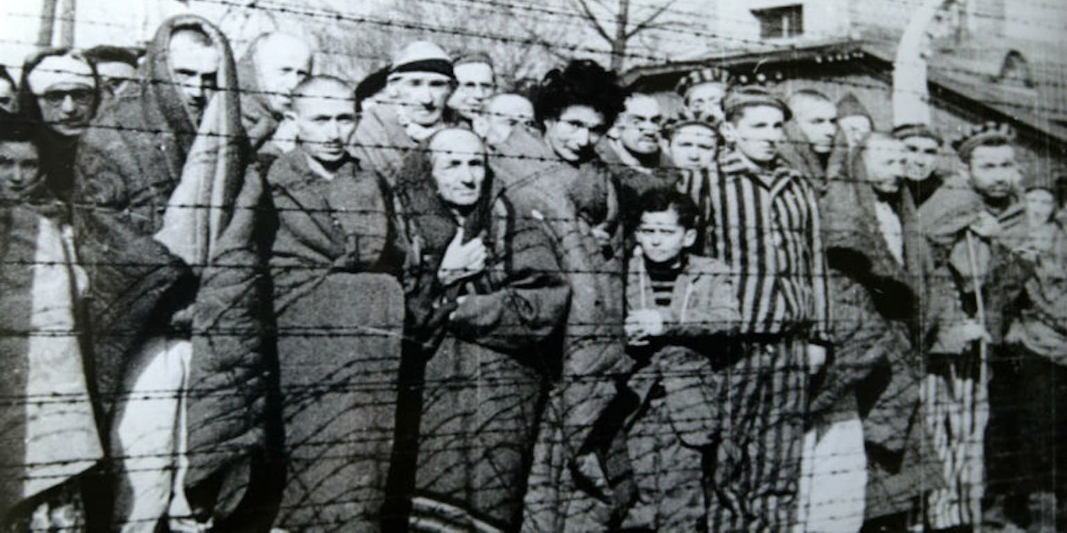 Een groep mensen staan achter prikkeldraad in het concentratiekamp in Auschwitz.