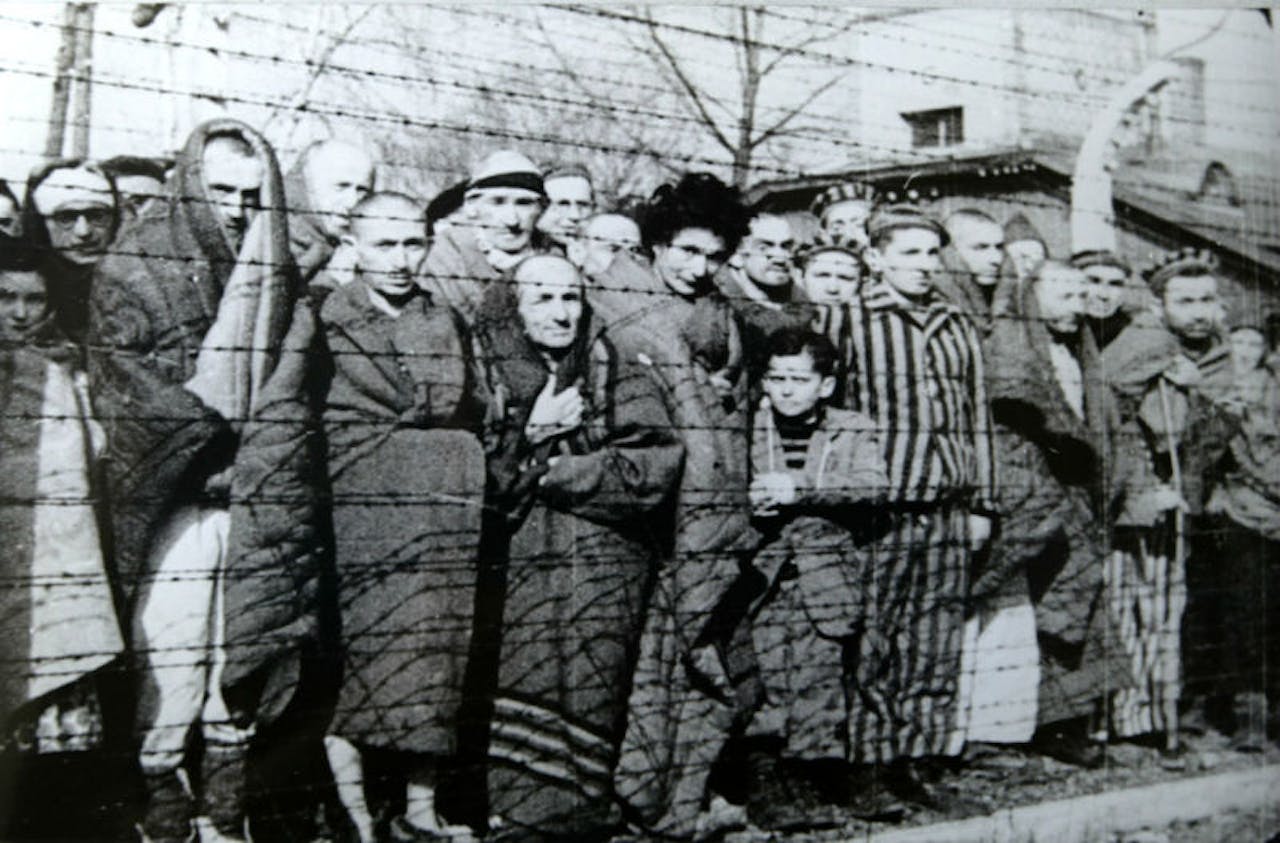 Een groep mensen staan achter prikkeldraad in het concentratiekamp in Auschwitz.