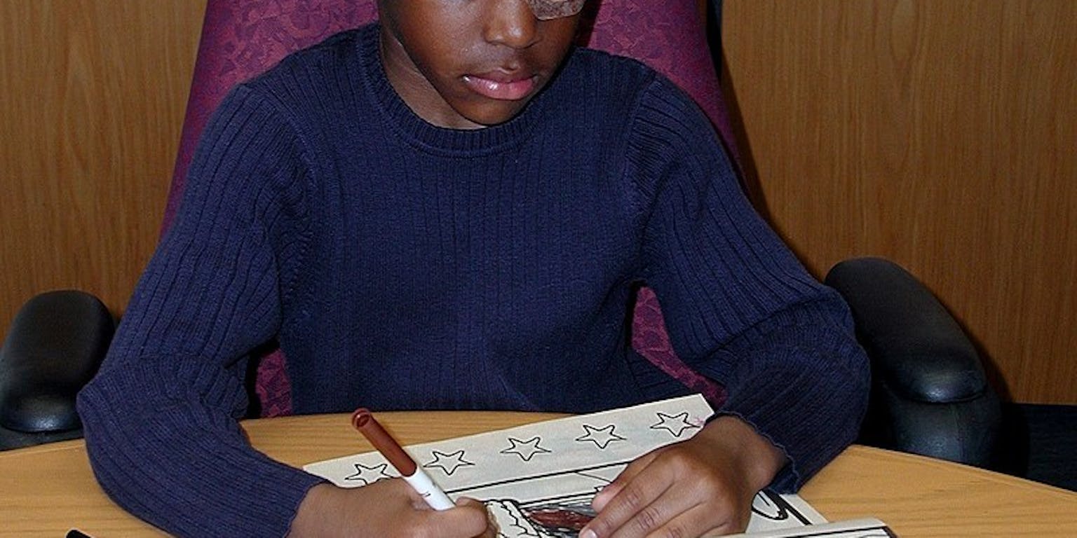 Een kind met één afgeplakt oog kleurt in een kleurboek.