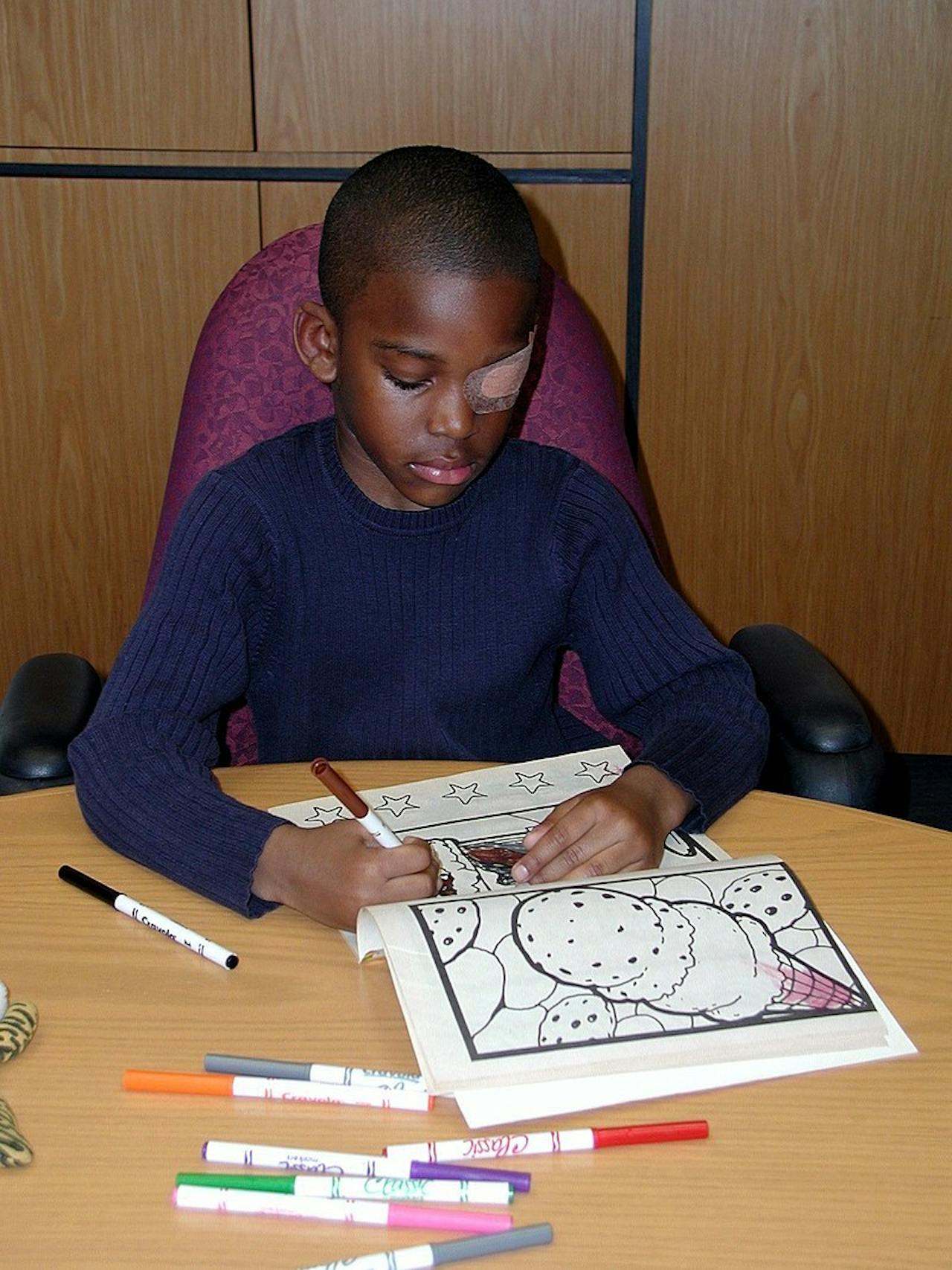Een kind met één afgeplakt oog kleurt in een kleurboek.