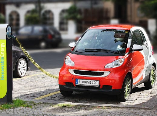 Rode elektrische auto die met een geel snoer oplaadt aan een laadpaal.