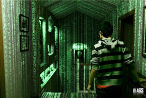 Een man in een gestreepte hoodie loopt door een gang met een groen scherm achter hem.