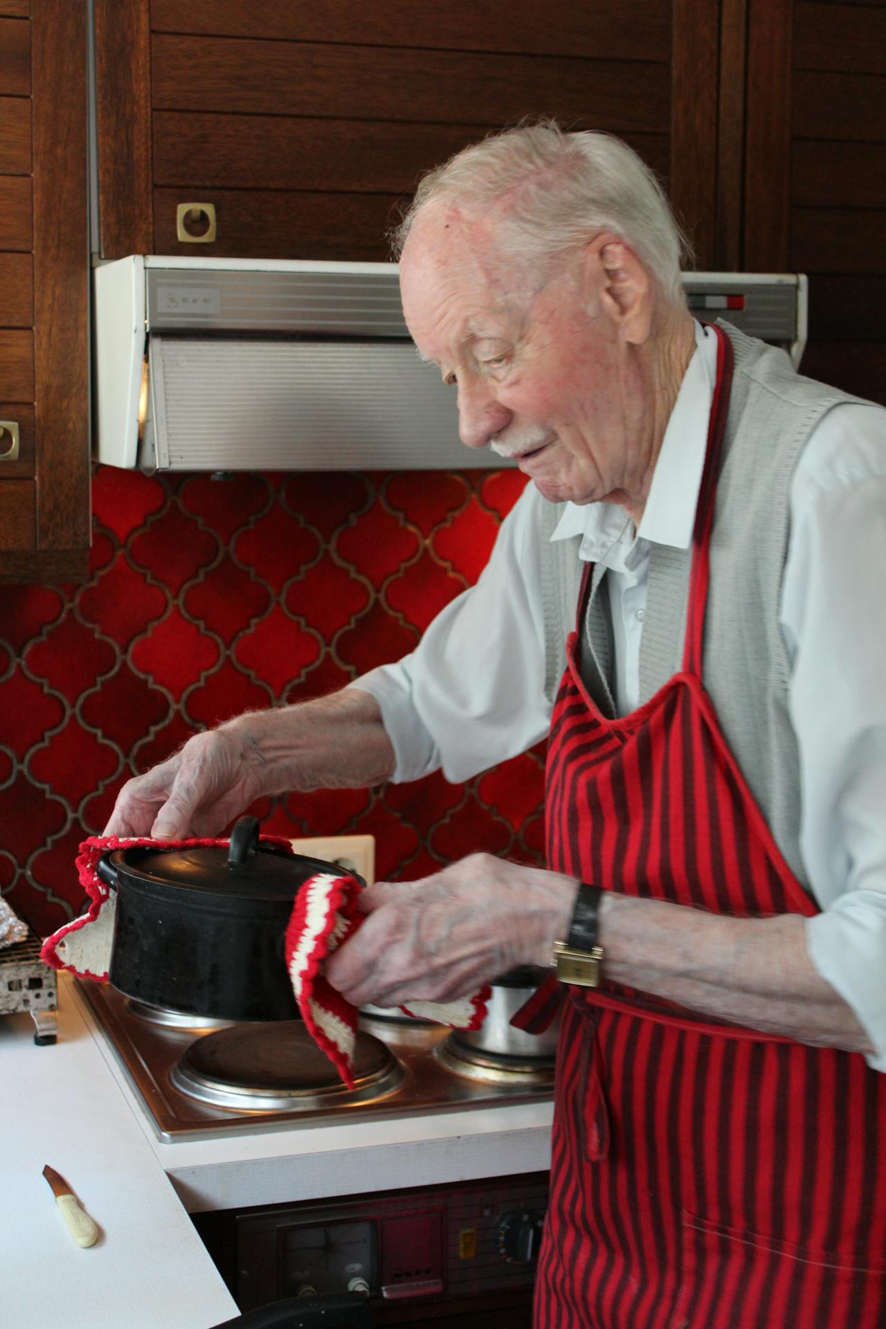 Een oudere man in een schort bereidt eten in een keuken.
