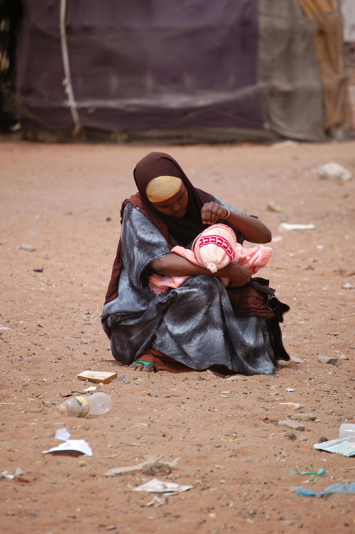 Een vrouw zit op de grond in het zand en houdt een baby vast.