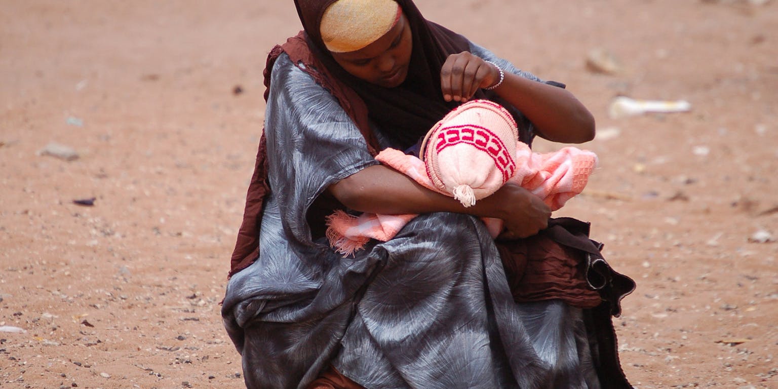 Een vrouw zit op de grond in het zand en houdt een baby vast.