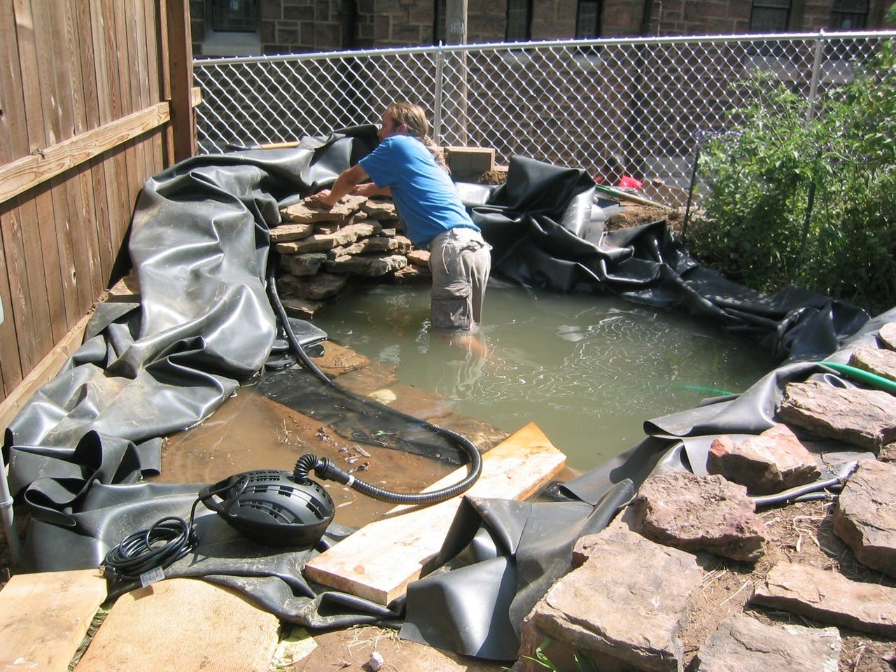 Een persoon is bezig met de installatie van een vijverpomp in een achtertuin.