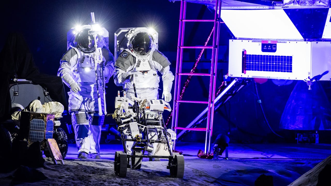 Twee astronauten lopen in blauwverlichte ruimte met een karretje.