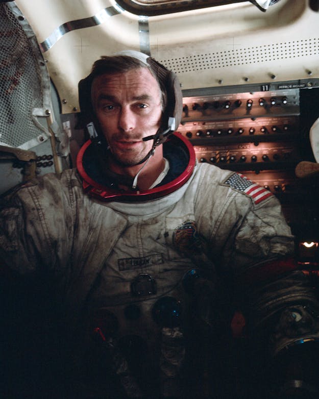 Astronaut Eugene Cernan komt in 1972 na een maanwandeling terug in de maanlander en zit onder het maanstof. Een astronaut zit zonder helm in een ruimtevaartuig. Zijn witte pak zit onder grijze en zwarte stof.