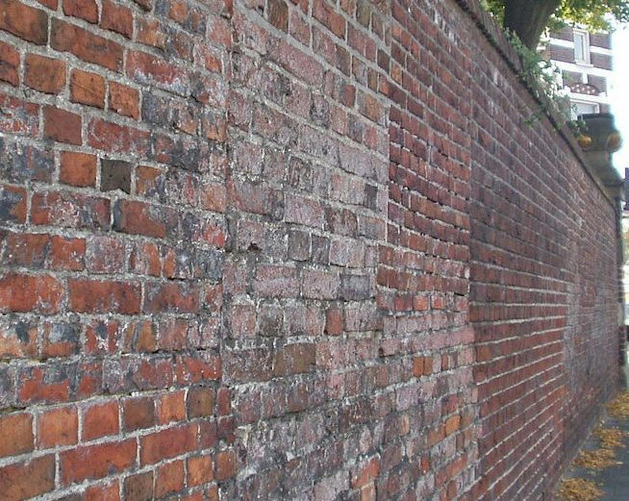 Een bakstenen muur naast een trottoir. Het metselwerk is aangetast.