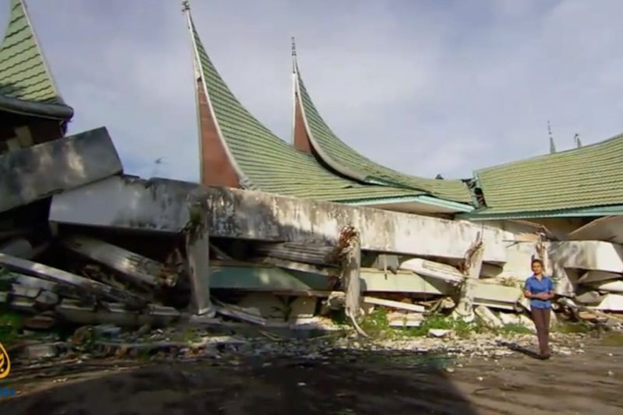 Een persoon staat voor een gebouw dat verwoest is door de aardbeving op Sumatra.