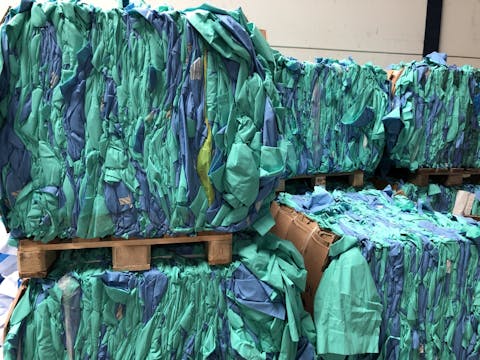De ingezamelde plastic afdekdoeken. Turquoise en blauwe plastic doeken zijn samengeperst tot vierkante pakketten op houten pallets.