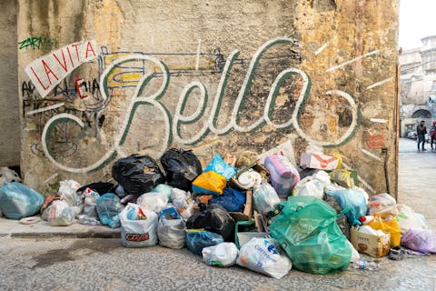 Het afvalprobleem in Palermo wordt veroorzaakt door een combinatie van factoren, waaronder een tekort aan middelen om de stad schoon te houden, de gevolgen van de privatisering en het faillissement van het staatsafvalbedrijf in het verleden, en de toenemende druk door toerisme. Rommelige stapeling van zwerfafval en vuilniszakken in een straat in Palermo