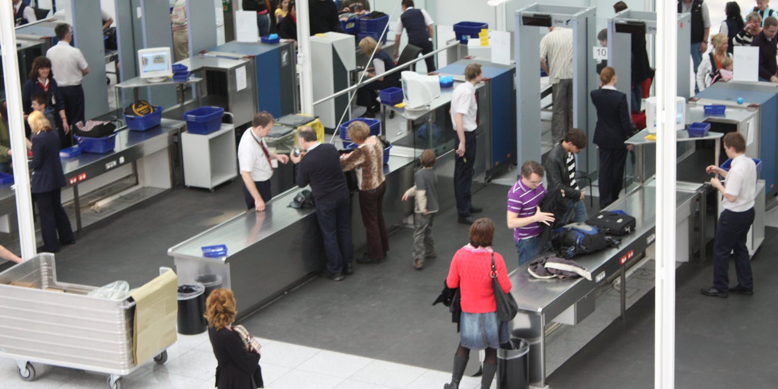 Een groep mensen staat in de wachtruimte van een luchthaven bij de tassencontrole.