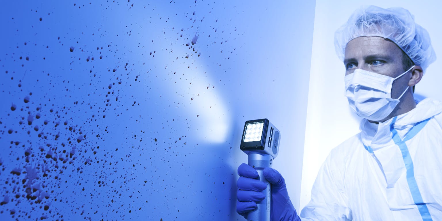 Een man in een beschermd pak analyseert bloedspoorpatronen op een plaats delict.