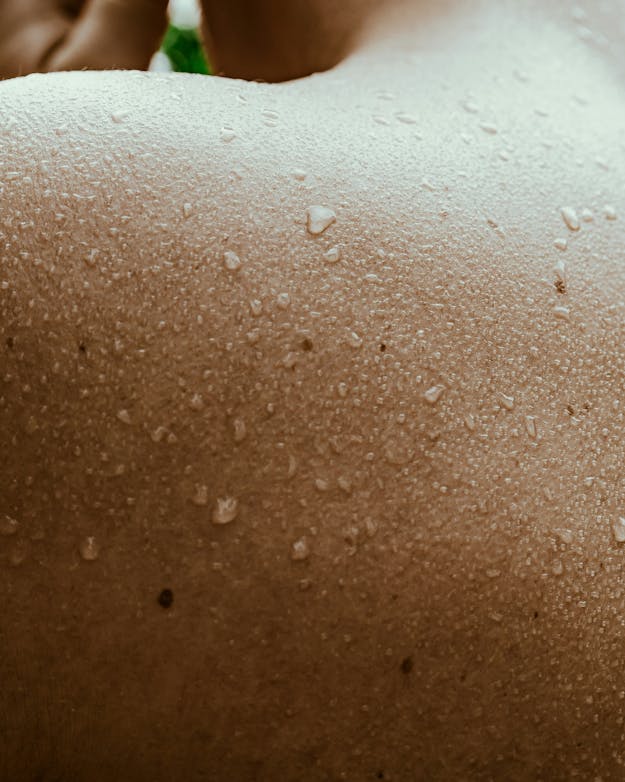 Wanneer afkoelen via vaatverwijding in de huid niet meer werkt, grijpt je lichaam naar een andere strategie: zweten. Closeup van een blote, bezwete schouder