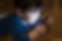 Een jongetje ligt op zijn buik en kijkt op een smartphone. Zijn gezicht is verlicht door het scherm.