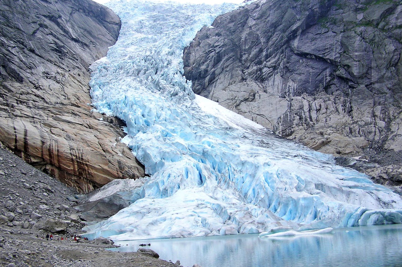 Een blauw-witte ijsmassa loopt tussen twee grijs-bruine rotspartijen door naar water.