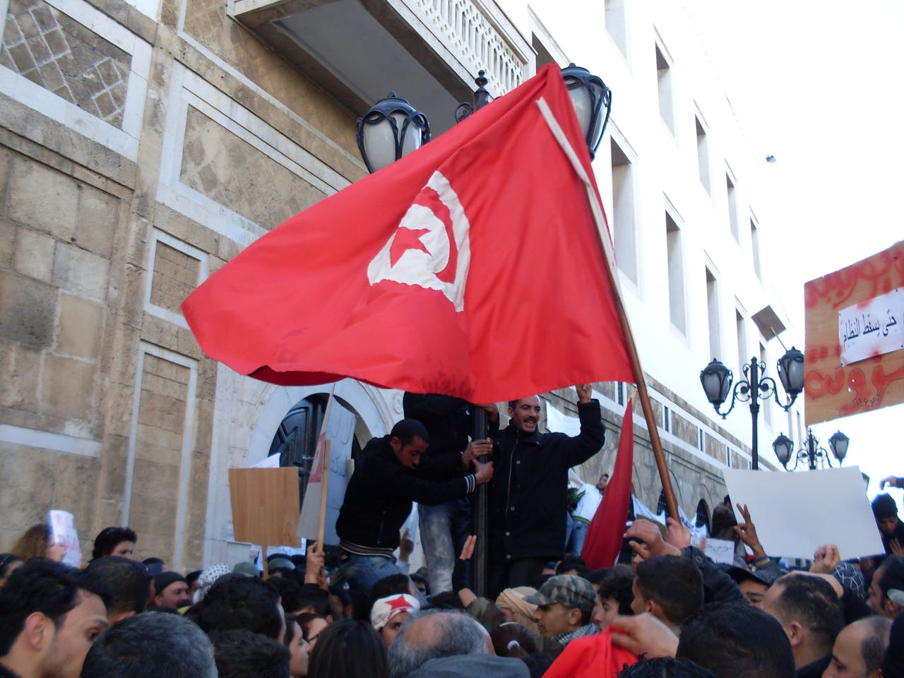 Demonstranten met een Tunesische vlag voor een overheidsgebouw tijdens de Jasmijnrevolutie.