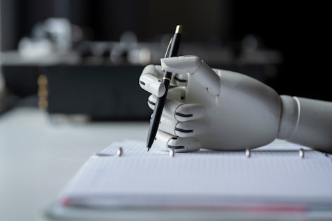 Een robothand die met een pen in een notitieboekje gaat schrijven.
