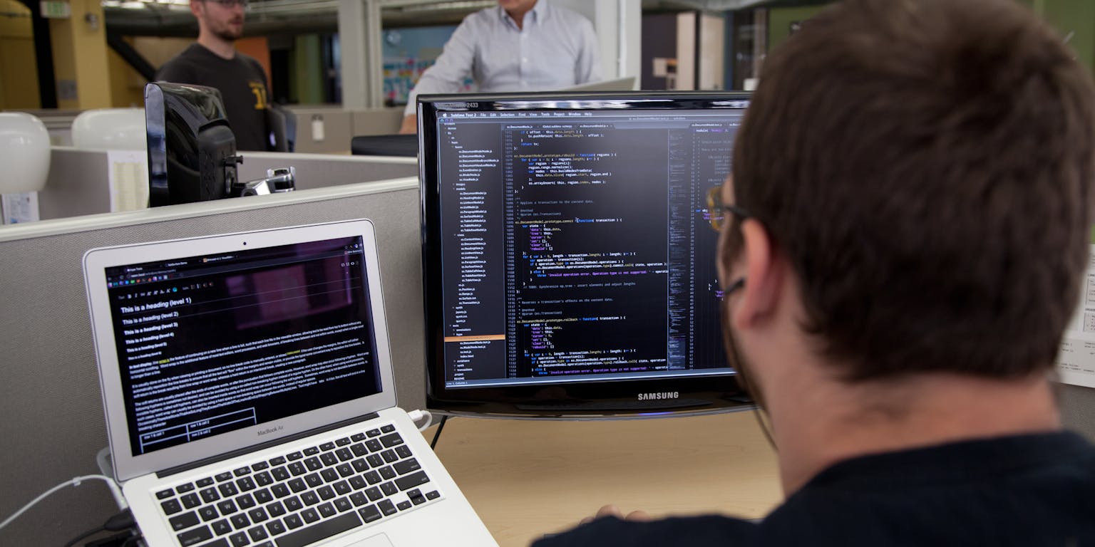 Een programmeur werkt aan een bureau achter zijn beeldschermen.