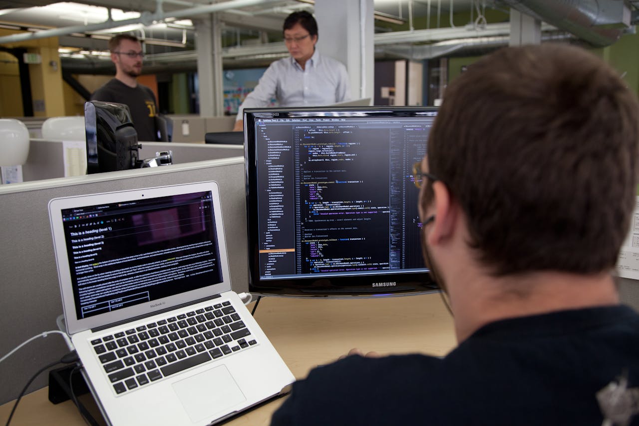 Een programmeur werkt aan een bureau achter zijn beeldschermen.