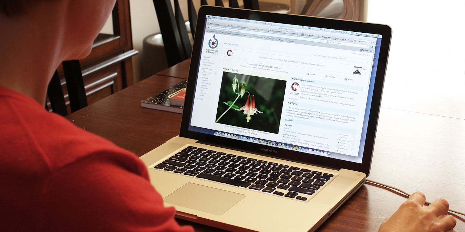 Een vrouw zit aan een tafel met een laptop erop. Op haar scherm is een bloem te zien.