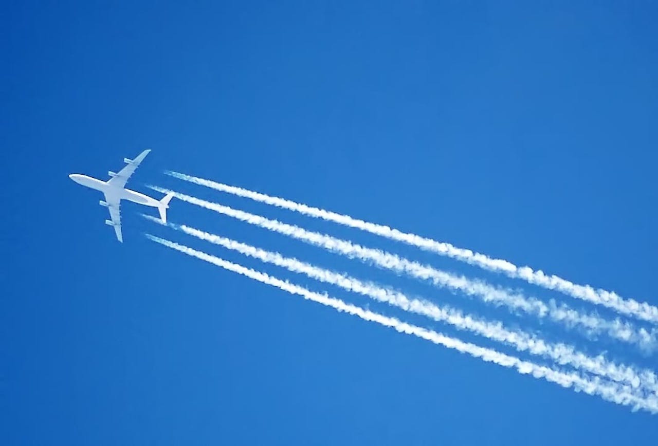 Een vliegtuig dat door een blauwe lucht vliegt en witte strepen achterlaat.