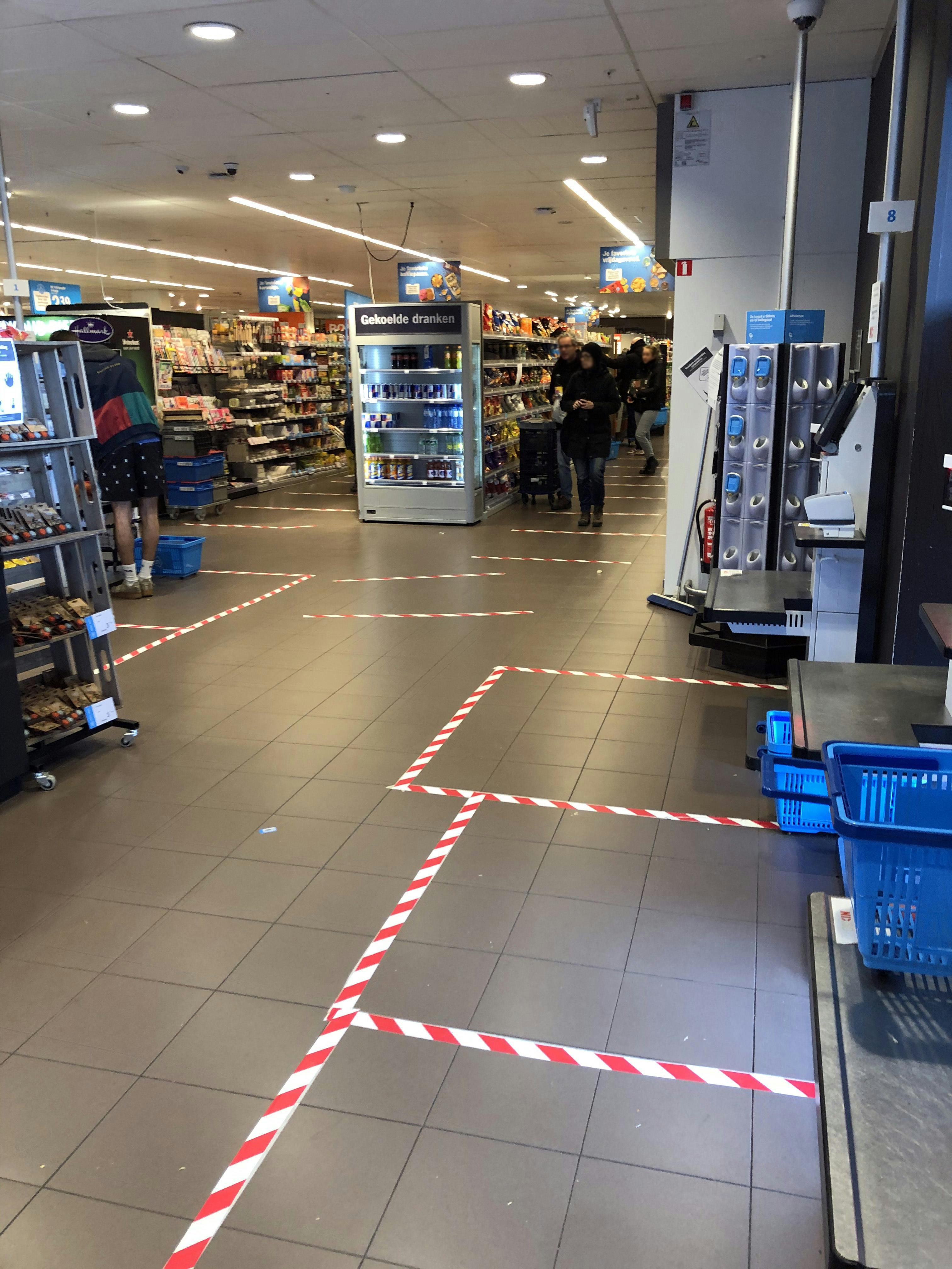 Een vloer in de supermarkt die zones markeert met rood-wit tape op de vloer. Het doel is om 1,5 meter afstand te kunnen houden in tijden van corona.