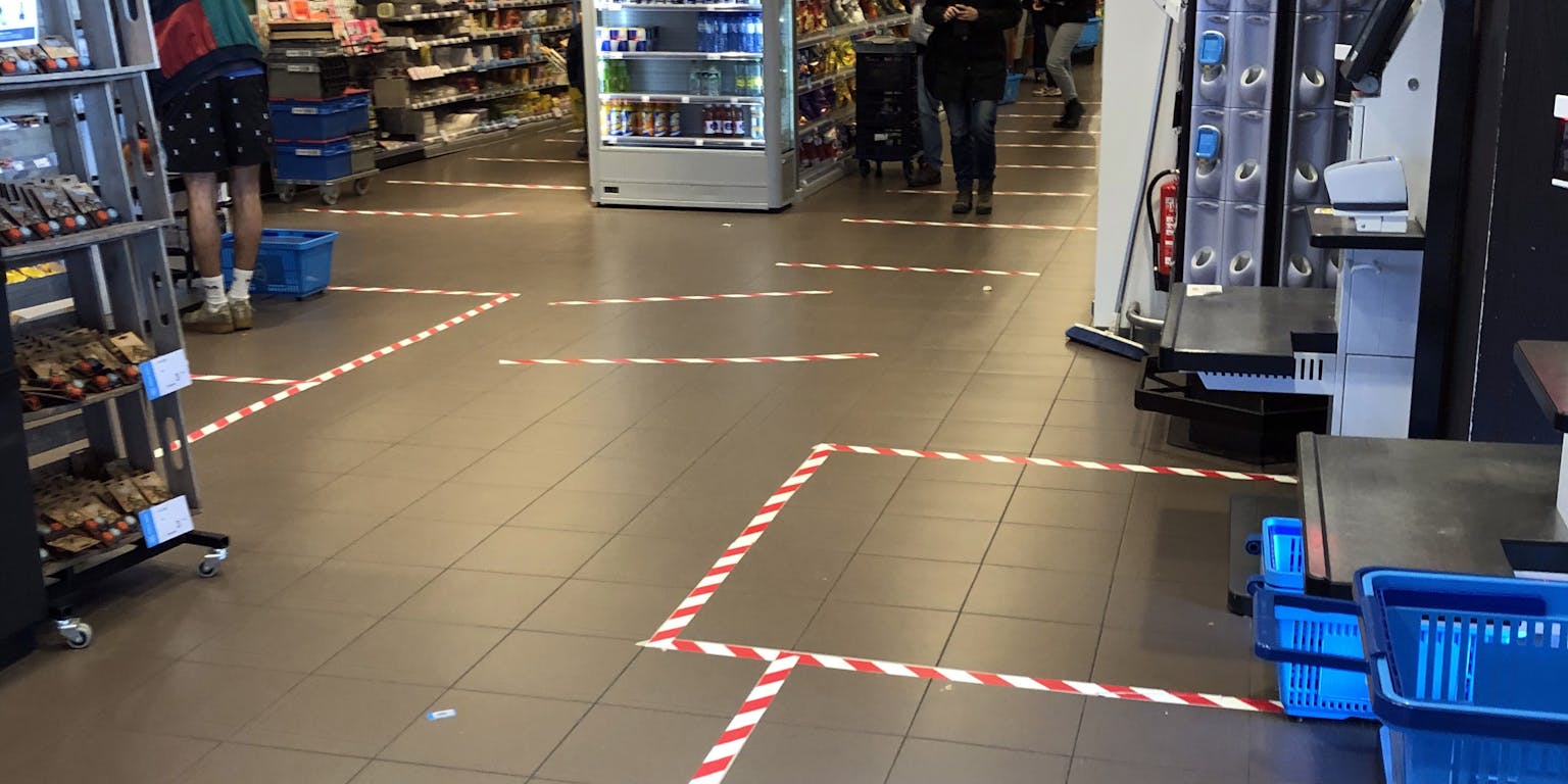 Een vloer in de supermarkt die zones markeert met rood-wit tape op de vloer. Het doel is om 1,5 meter afstand te kunnen houden in tijden van corona.
