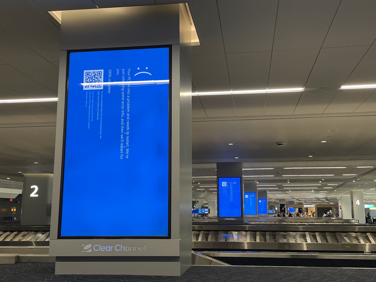 Lege bagagebanden in de aankomsthal van een vliegveld. Op de tv-schermen bij de banden zijn blauwe schermen met een foutmelding te zien.