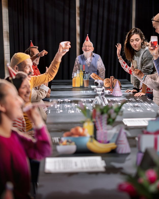 Mensen van allerlei leeftijden zitten aan tafel met feesthoedjes op, als in een kringverjaardag Mensen van allerlei leeftijden zitten aan tafel met feesthoedjes op, als in een kringverjaardag