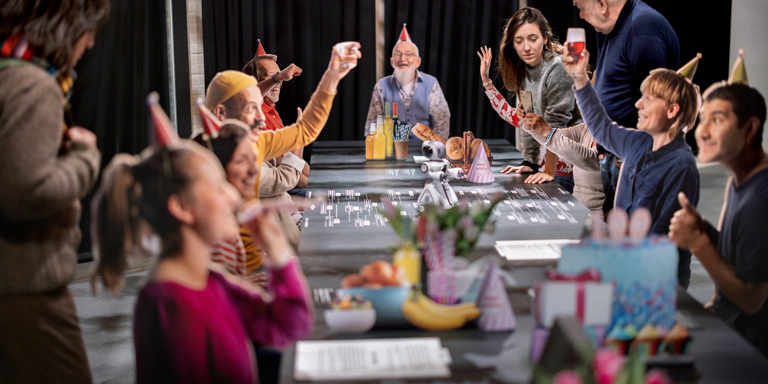 Mensen van allerlei leeftijden zitten aan tafel met feesthoedjes op, als in een kringverjaardag