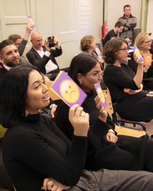 Deelnemers van de DNA Dialoog Rotterdam stemmen over een stelling met kaarten met daarop lachende of fronsende smileys.