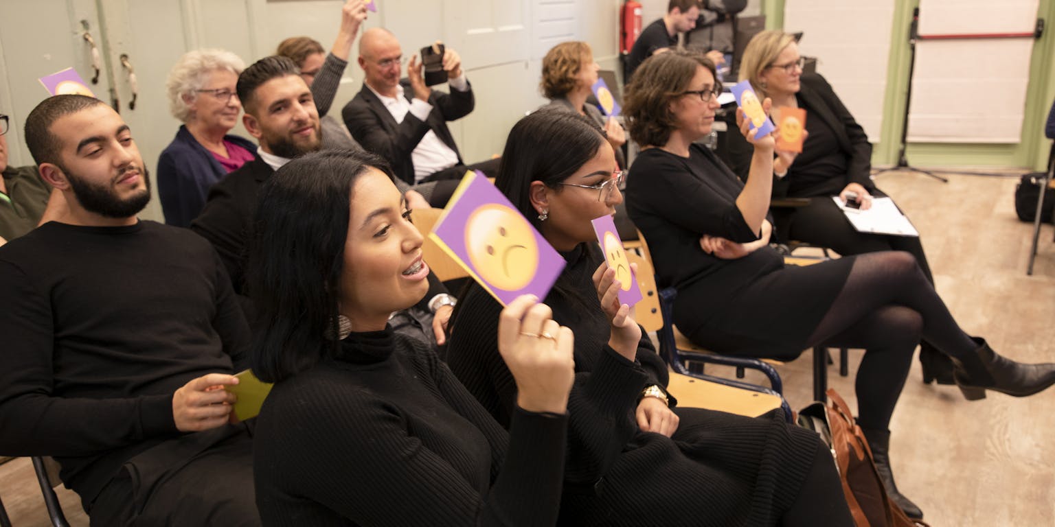 Deelnemers van de DNA Dialoog Rotterdam stemmen over een stelling met kaarten met daarop lachende of fronsende smileys.