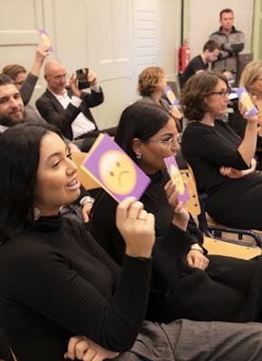 Deelnemers van de DNA Dialoog Rotterdam stemmen over een stelling met kaarten met daarop lachende of fronsende smileys.