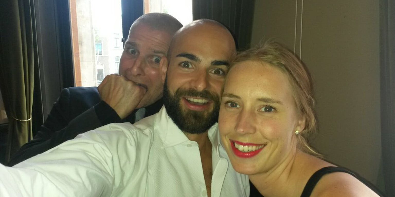 Twee mannen en een vrouw maken een selfie in een hotelkamer.