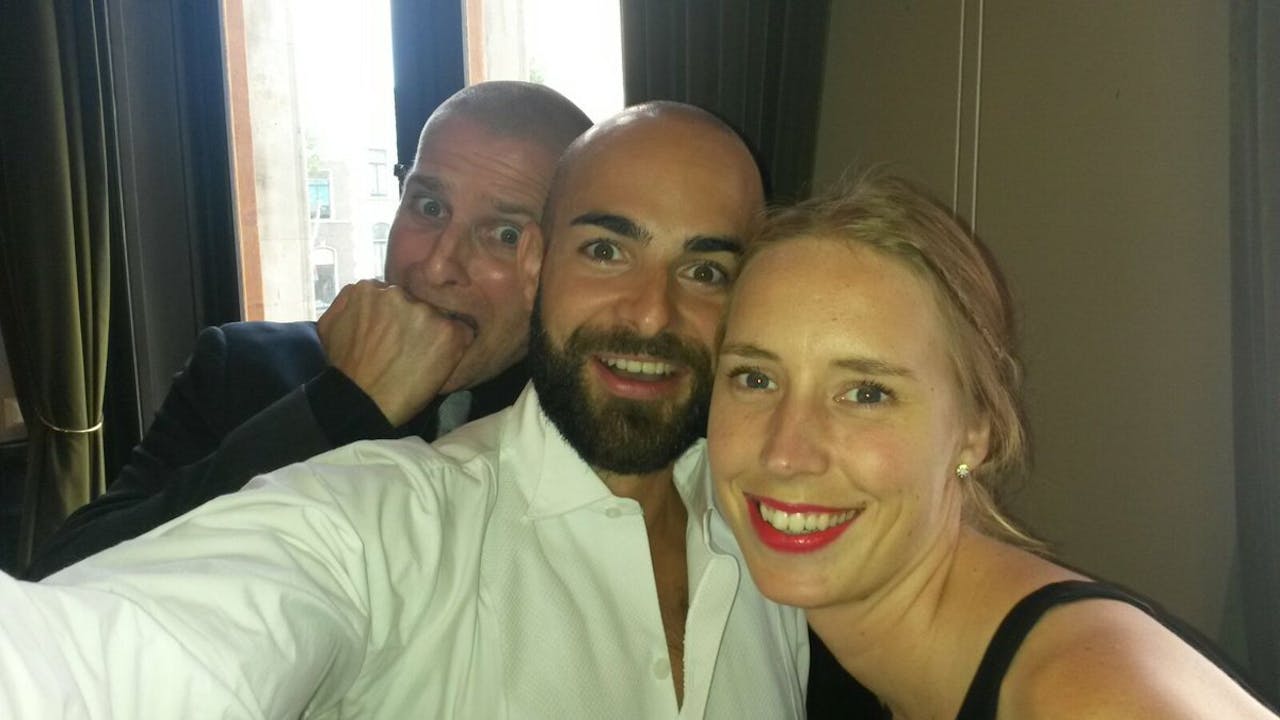 Twee mannen en een vrouw maken een selfie in een hotelkamer.
