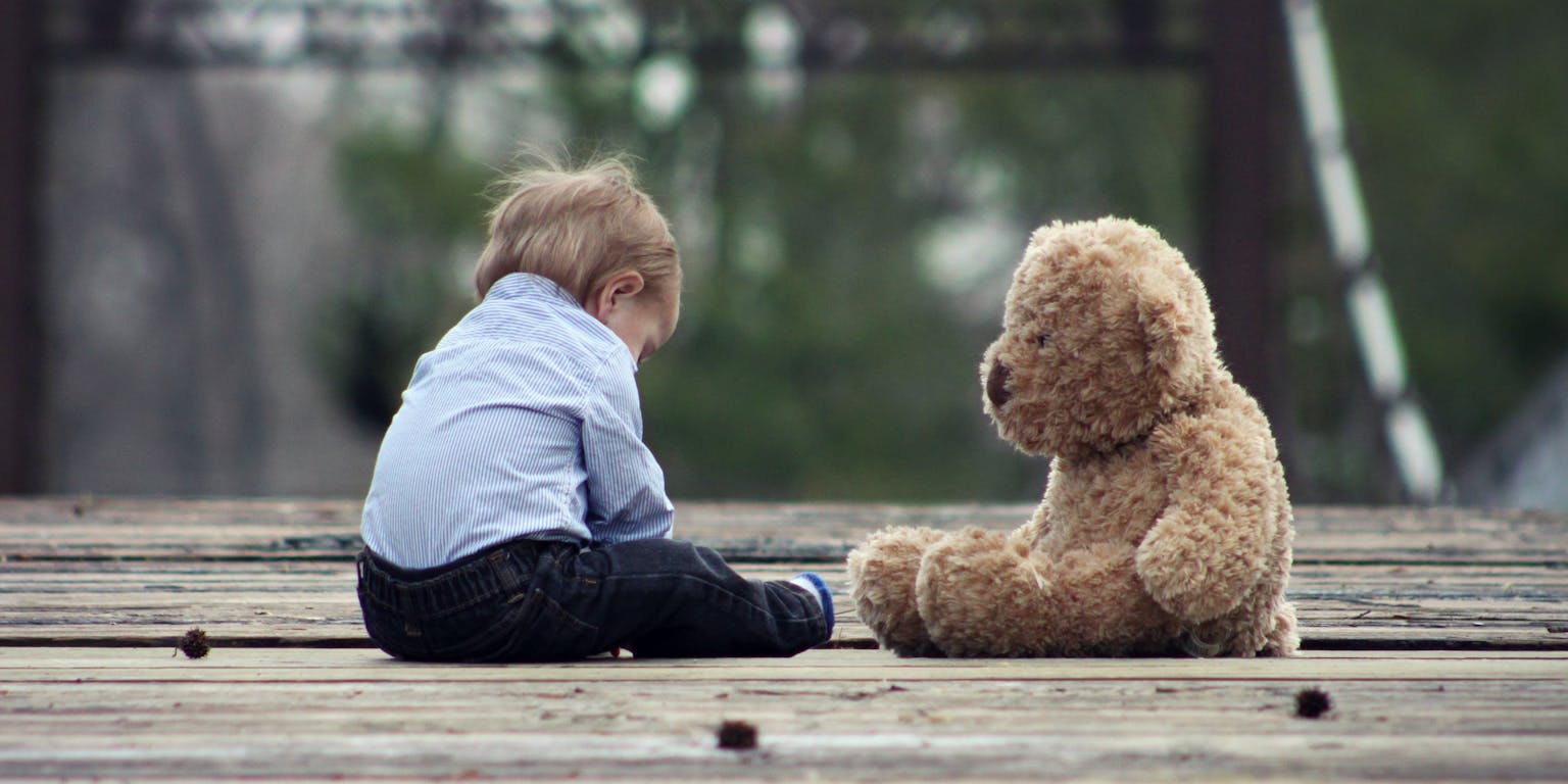 Een kind zit op de grond naast een teddybeer.