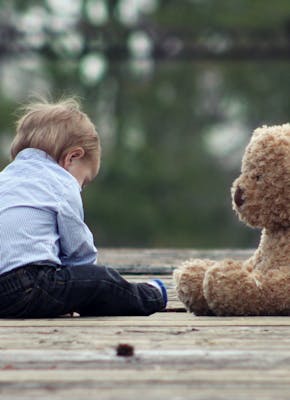 Een kind zit op de grond naast een teddybeer.