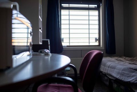Als een dader na een celstraf vrijkomt, voelt het slachtoffer zich vaak alsnog onveilig. Cel in een gevangenis met een raam met tralies ervoor, een bed en een bureautje met bureaustoel en magnetron