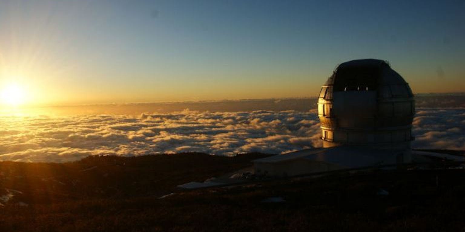Een foto van de Gran Tecan telescoop op La Palma boven de wolken. De zon is duidelijk zichtbaar.