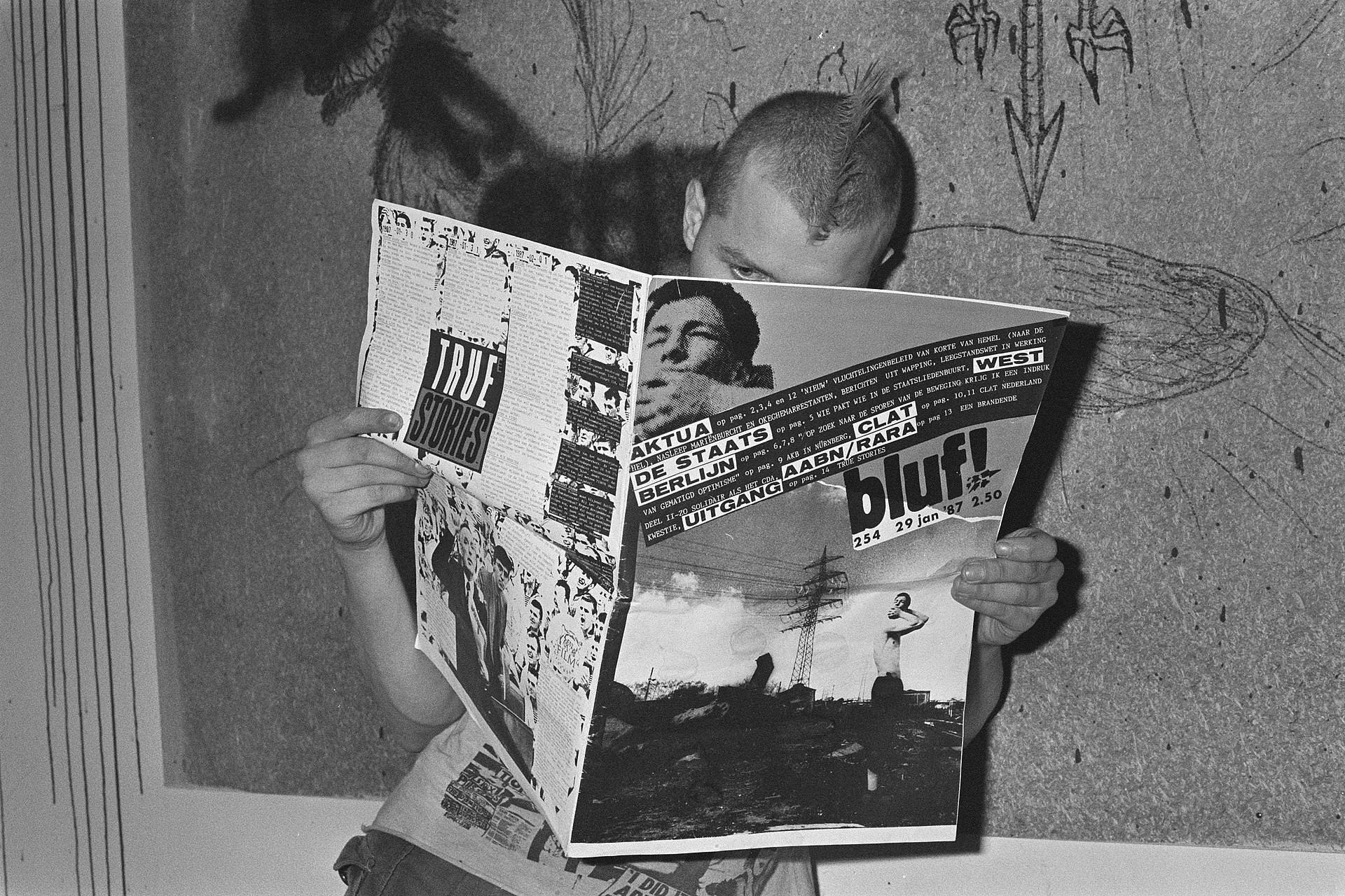 Man met hanenkam houdt opengeslagen krant voor zich (zwart-witfoto).