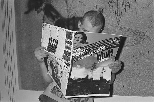 Man met hanenkam houdt opengeslagen krant voor zich (zwart-witfoto).